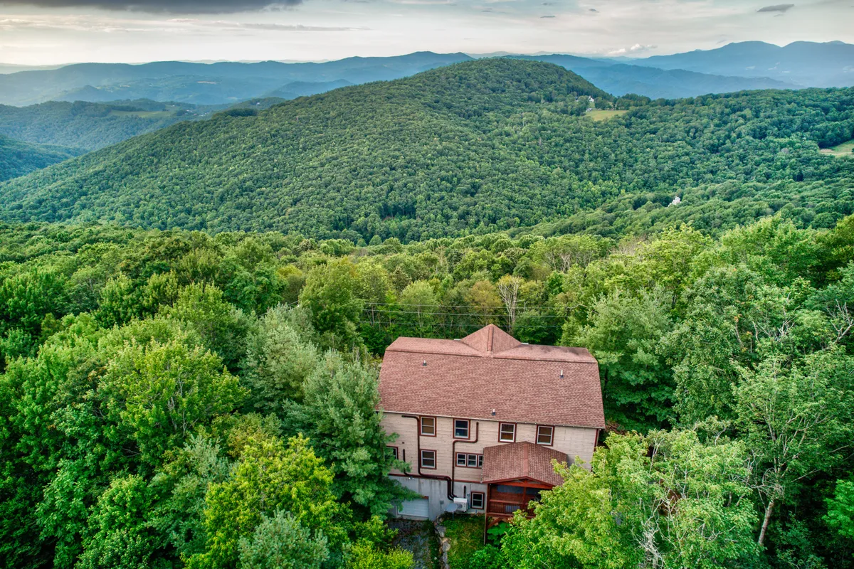 This exterior image captures the house surrounded by trees with mountains in the background, evoking a tranquil, adventure-filled mountain getaway. The setting hints at the home's proximity to nature trails and outdoor activities, with the house nestled in a landscape perfect for exploration and group experiences.