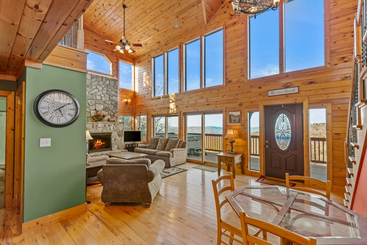 A welcoming seating area arranged near a stone fireplace, complemented by a large dining table and expansive windows that showcase scenic vistas. The layout invites relaxation, conversation, and shared experiences, all bathed in warm, natural light.