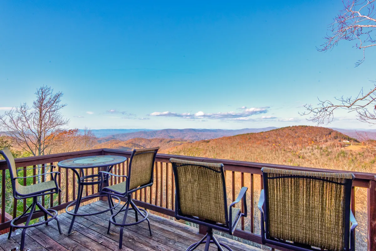A serene deck setting with comfortable chairs, a table, and unobstructed mountain views. The deck is inviting for both morning coffee and evening relaxation, with the soft light emphasizing the vibrant seasonal colors of the landscape. The image exudes a tranquil, restful mood, ideal for enjoying nature at any time of day.