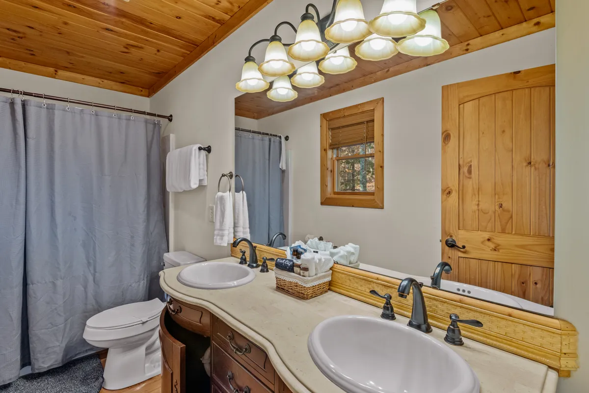 A modern bathroom with a double sink vanity, wooden accents, decorative lighting, and a shower curtain. The space is calm and well-appointed, ideal for morning routines or unwinding after a busy day.