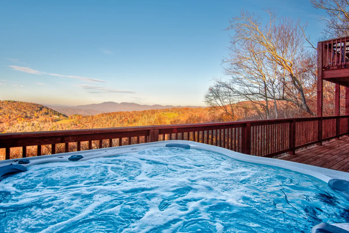 A spacious deck with a hot tub overlooks sweeping mountain views, surrounded by trees. The deck is furnished for relaxation and socializing, creating an inviting space to enjoy the outdoors. The scene captures the serene atmosphere and provides plenty of area for both guests and their pets to unwind together.