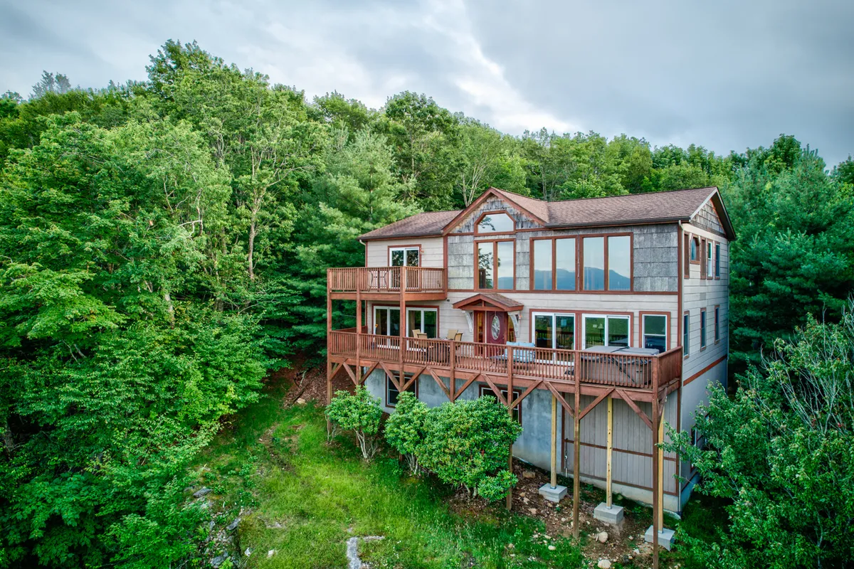 The exterior shot showcases the home's large windows, a wooden deck, and welcoming entrance, set against the natural landscape. The deck is ideal for group gatherings, barbecues, and relaxation after a day of adventure, tying into the narrative about communal experiences and family fun.