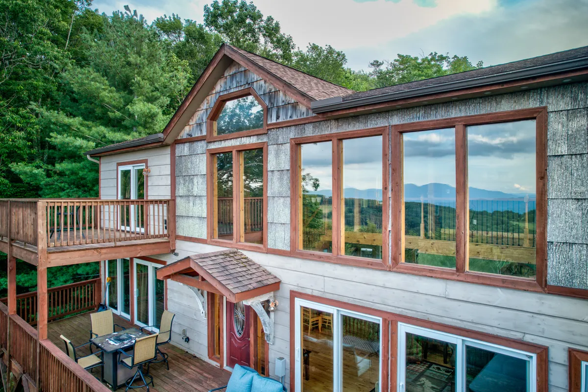 The image showcases the home's inviting wooden deck with ample seating, panoramic mountain views, and large windows that hint at a bright, spacious interior. The scene is set for outdoor dining and relaxation, with the backdrop of Beech Mountain's rolling peaks at sunrise.